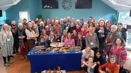 A large group of people, smiling, stand around a table with natural objects