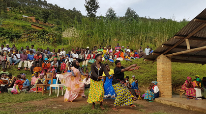 A photo of four people dancing in front of several dozen people seated outside.
