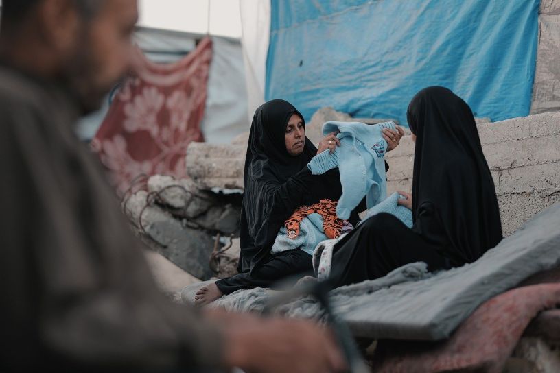 Two women in rubble holding baby clothes