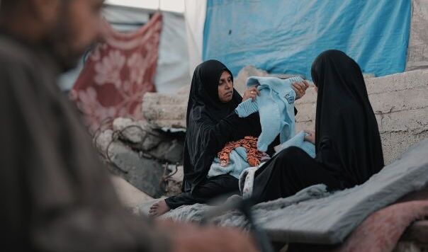 Two women sitting on rubble holding baby clothes
