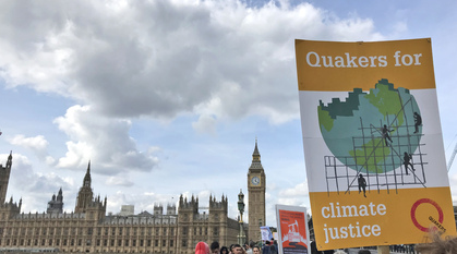 A person holds up a Quakers for climate justice placard on Westminster Bridge with parliament in the background