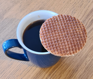 A cup of black Colombian coffee with an as yet unbitten stroopwafel