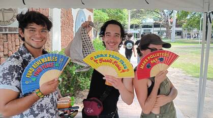 3 people holding up fans with messages on: Make Polluters Pay, Fund Renewables Fund Peace, and Break Free from Fossil Fuels