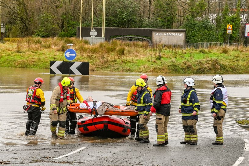 Firemen carry an elderly lady on a stretcher next to flood