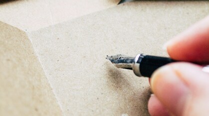 A hand holds a fountain pen over a piece of blank paper, ready to start writing